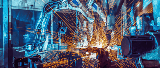 Robotic CNC welding machine in a factory setting with sparks flying, indicating automation and technology.