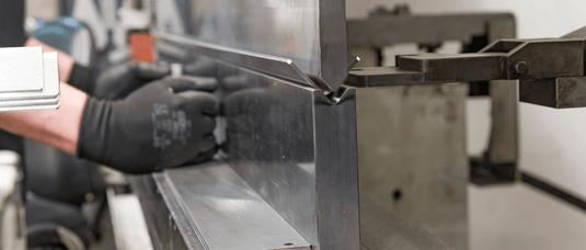 Close-up of a CNC press brake bending stainless steel sheet, showing precise metal forming with operator handling the process.