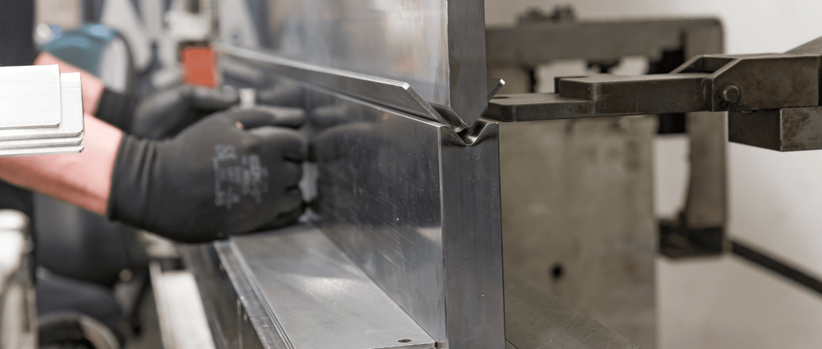 Close-up of a CNC press brake bending stainless steel sheet, showing precise metal forming with operator handling the process.