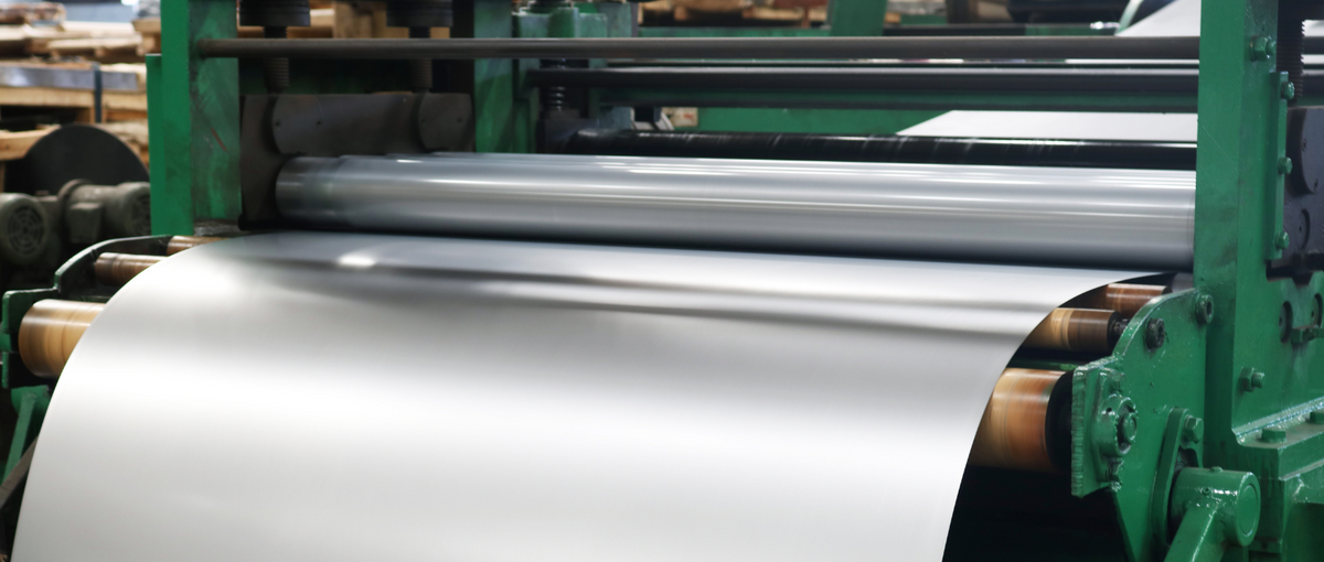 Stainless steel sheet being processed through an industrial plate rolling machine for precision forming.